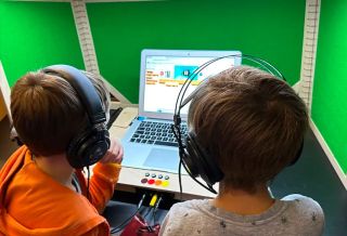Online muzieksymposium - 2 kinderen kijken en luisteren met koptelefoon naar beeld op laptop